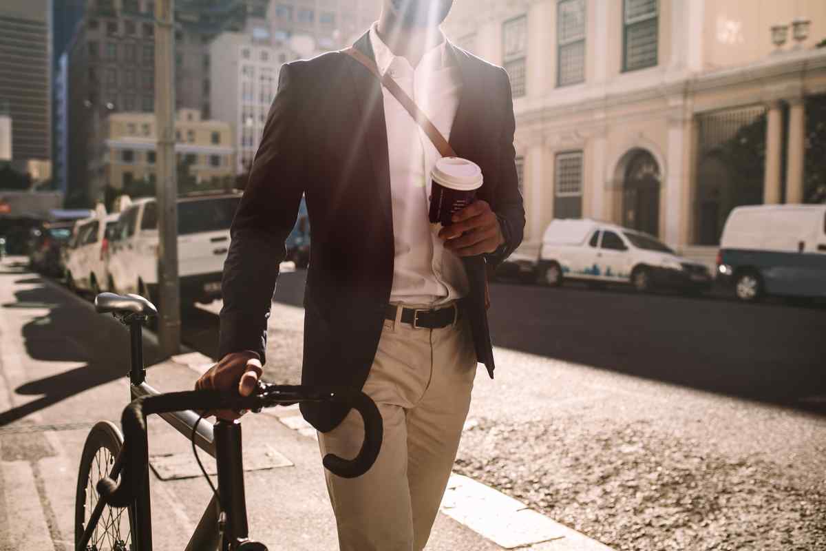 Man walking with bike and holding coffee.