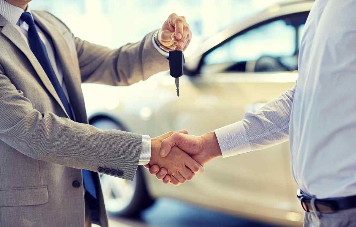 Car salesperson handing keys to buyer and shaking hands