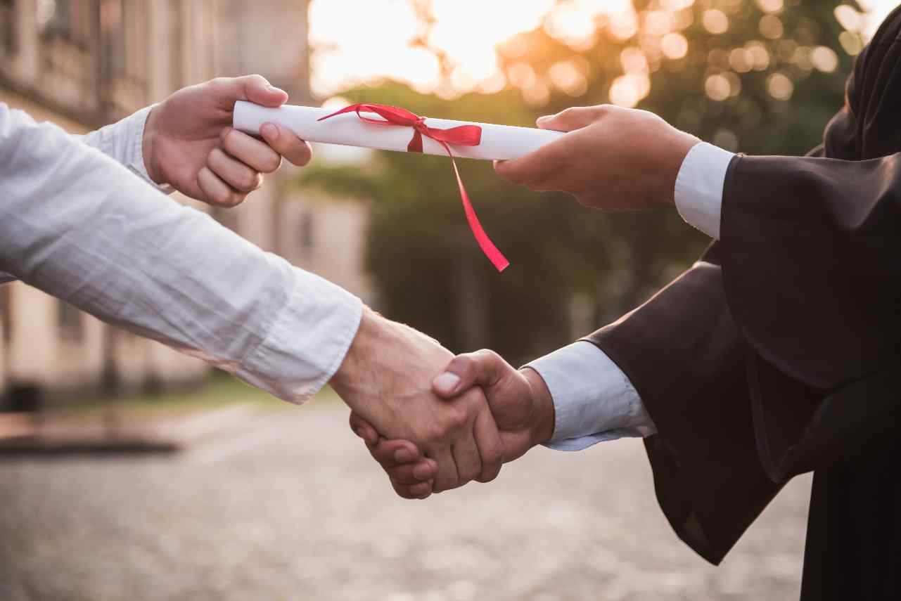 Close up on college graduate shaking hands with Dean and receiving diploma