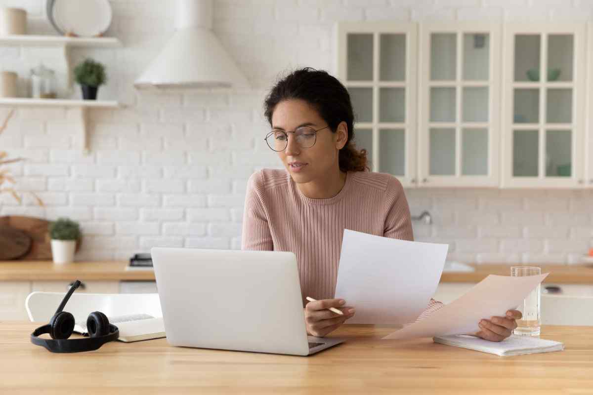Woman comparing documents next to laptop.