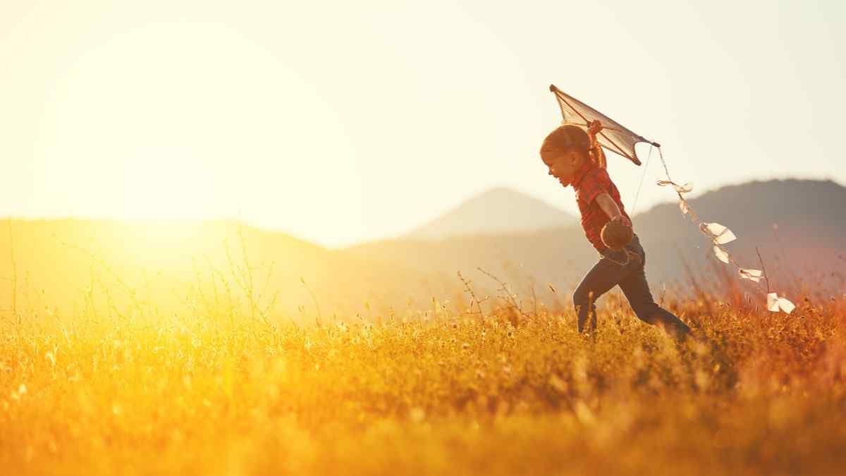 A young girl running through a field with a kite in her hand.