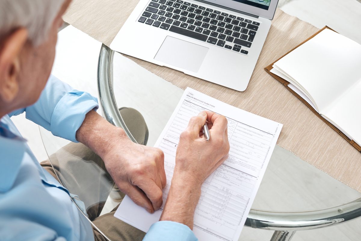 Man filling out forms in front of laptop.