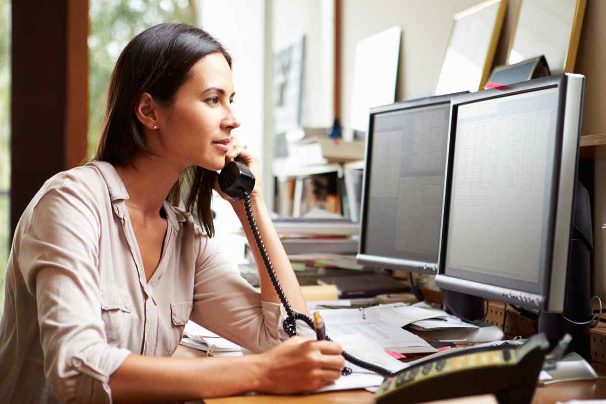 Woman making a phone call while looking at her desktop computer.