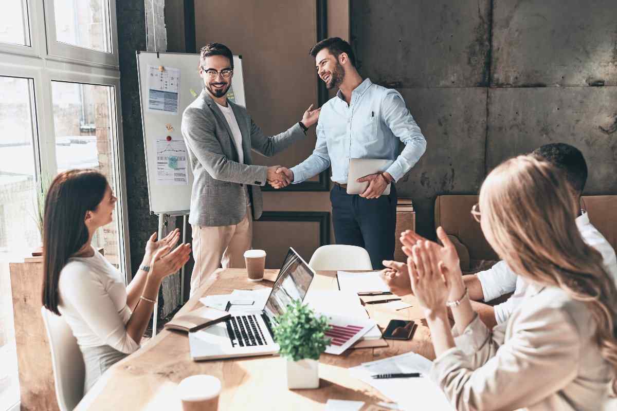 Professional shaking hands with manager, and other employees clapping during meeting 