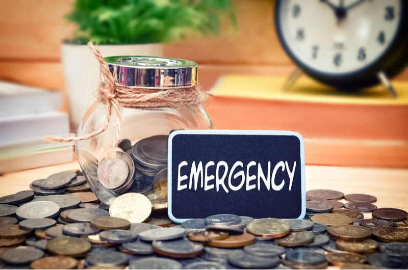 Amidst the coins surrounding a jar half-fulled with coins is a card that says 'Emergency.'